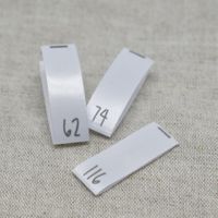 Närbild på tre vita vävda storleksetiketter i satin med tryckta siffror 62, 74 och 116, från artikeln Storlekstag 074 – Vävd Etikett i Satin.