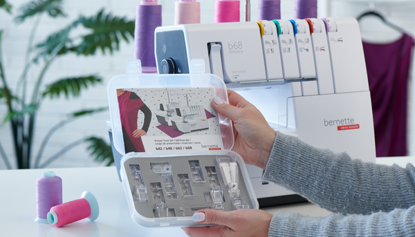 Pressarfotset upp&ouml;ppnad som h&aring;lls upp av en m&auml;nniskas arm, i bakgrunden syns bernette b68 overlockmaskinen, lite tr&aring;drullar, en monstrerav&auml;xt och en kl&auml;nning.