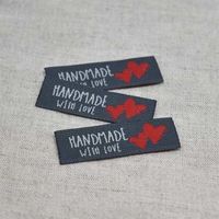 N&auml;rbild p&aring; svarta v&auml;vda etiketter med vit text "Handmade with love" och tv&aring; r&ouml;da hj&auml;rtan, fr&aring;n artikeln V&auml;vd Etikett Handmade With Love R&ouml;d.