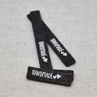 Närbild på svarta filtetiketter med vit text "HANDMADE" och hjärtan, från artikeln Filtlabel Handmade Svart/Vit – 10-pack 