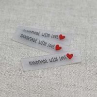 Närbild på transparent silikonetikett med texten "Handmade with love" och ett rött hjärta, från artikeln Silikon Etikett “Handmade With Love” Röd 10‑pack.