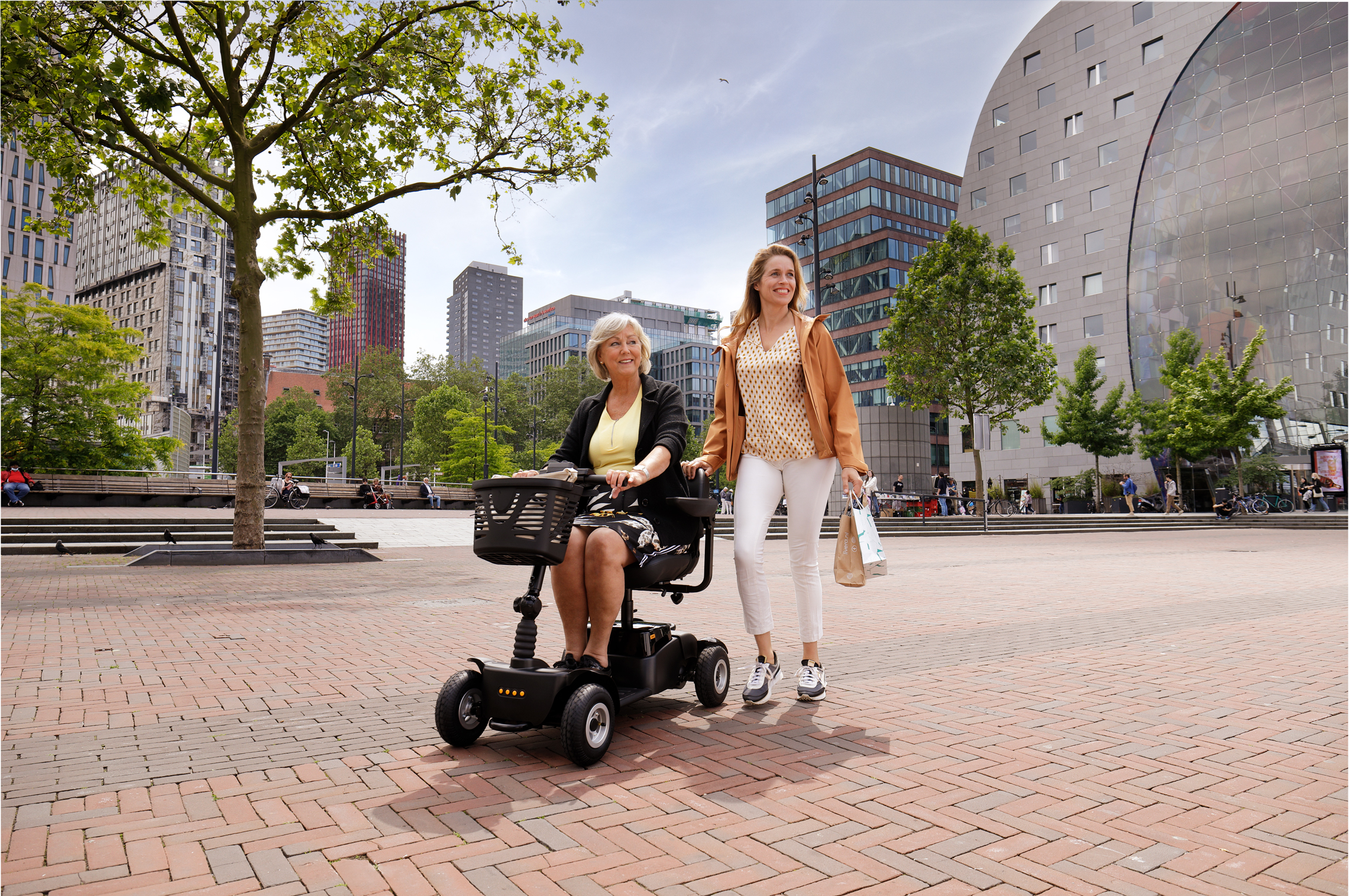 två kvinnor. En på en scooter och den andra går bredvid